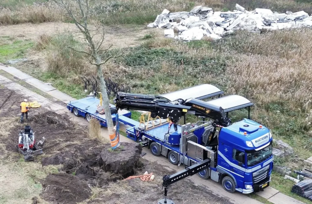 Luchtfoto van een kraanwagen die een boom op een oplegger laadt
