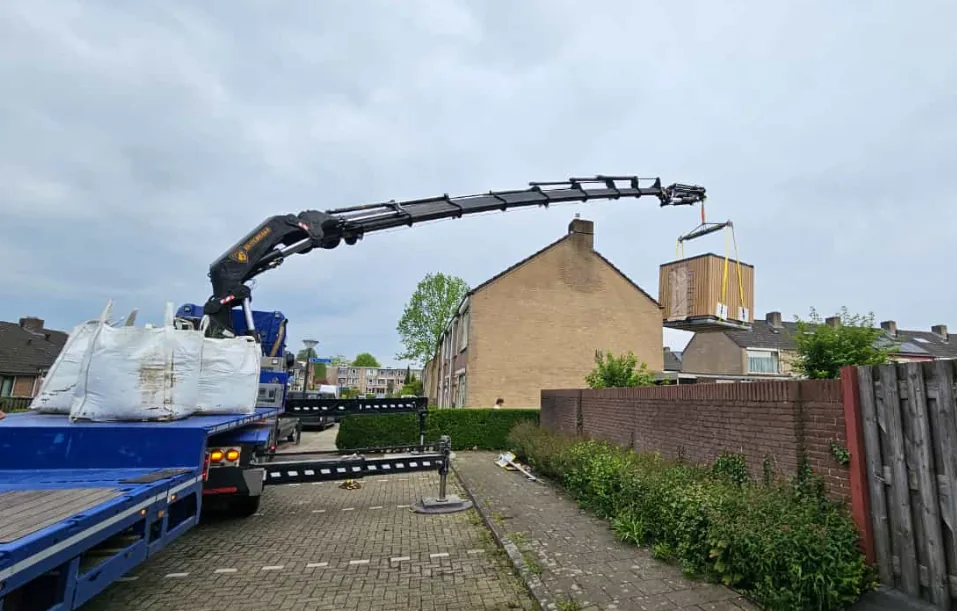 Kraanwagen hijst een container over een woning heen