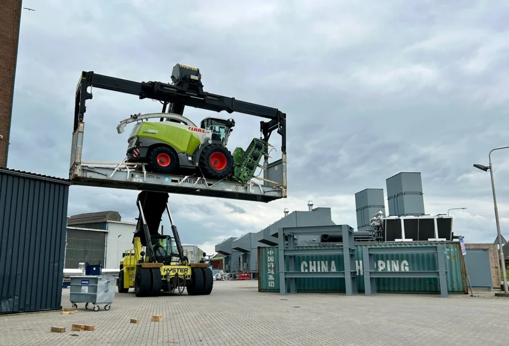 Reachstacker tilt een flatrack met een Claas hakselaar op het terrein in Alblasserdam