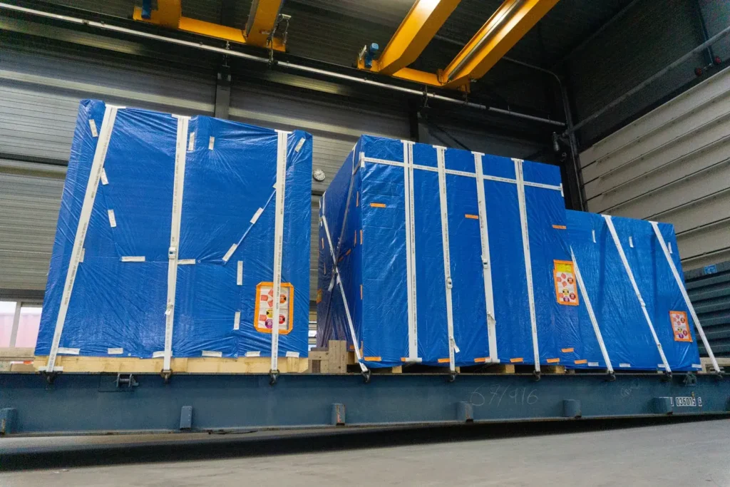 In blauwe folie verpakte kisten vastgezet op een flatrack